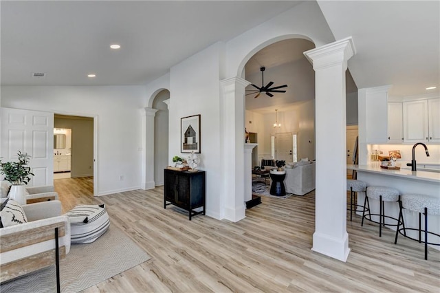 living room with lofted ceiling, sink, light wood-type flooring, ceiling fan, and decorative columns