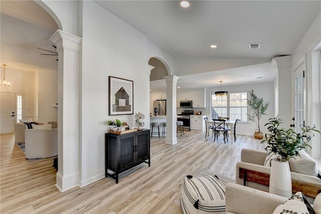 living room with decorative columns, lofted ceiling, and light hardwood / wood-style floors