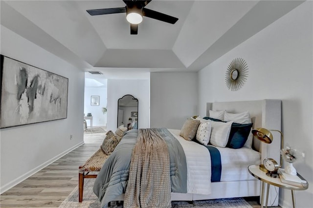 bedroom featuring ceiling fan, a raised ceiling, and light wood-type flooring