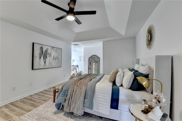 bedroom with a tray ceiling, ceiling fan, and light hardwood / wood-style flooring