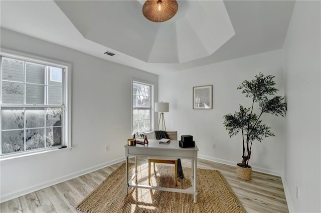 home office with light wood-type flooring and a tray ceiling