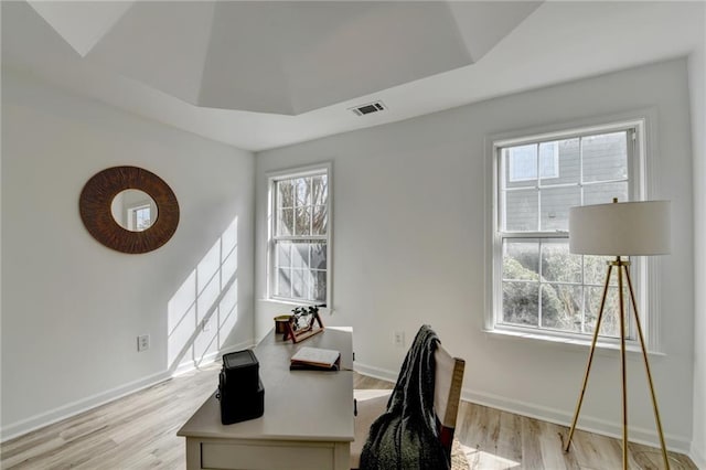 office area with a tray ceiling and light wood-type flooring