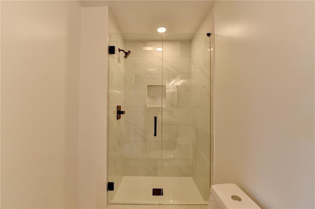 bathroom featuring a shower with door and toilet