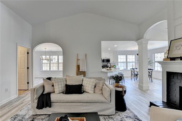 living room featuring decorative columns, sink, high vaulted ceiling, and light hardwood / wood-style flooring