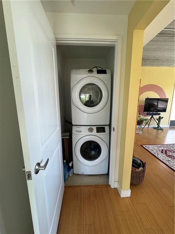 clothes washing area with light wood-type flooring and stacked washer and dryer