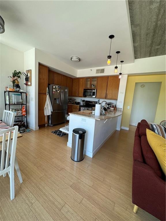 kitchen featuring pendant lighting, light hardwood / wood-style flooring, stainless steel appliances, light stone counters, and kitchen peninsula