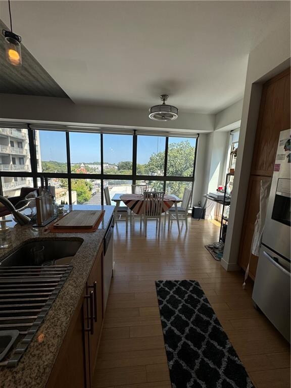 kitchen featuring stainless steel fridge, hanging light fixtures, dark wood-type flooring, sink, and dark stone countertops