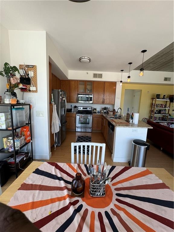 kitchen with light wood-type flooring, stainless steel appliances, sink, kitchen peninsula, and pendant lighting