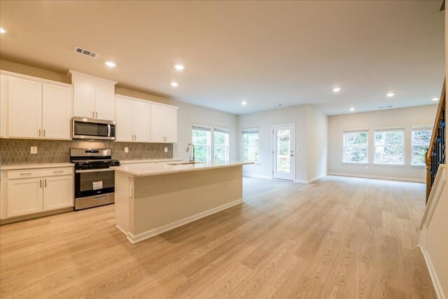 kitchen featuring decorative backsplash, an island with sink, light hardwood / wood-style floors, white cabinetry, and stainless steel appliances