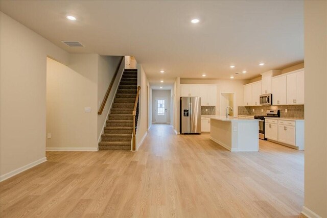 kitchen with sink, light hardwood / wood-style flooring, an island with sink, white cabinets, and appliances with stainless steel finishes