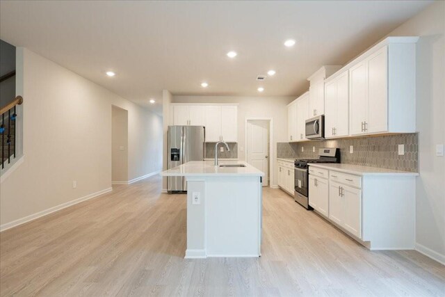 kitchen with white cabinetry, sink, light hardwood / wood-style flooring, a kitchen island with sink, and appliances with stainless steel finishes