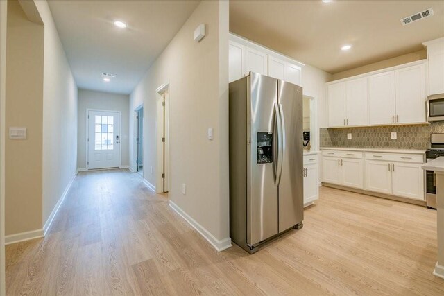 kitchen with light wood-type flooring, white cabinetry, stainless steel appliances, and tasteful backsplash