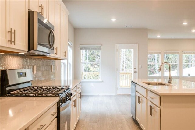 kitchen with sink, light stone counters, light hardwood / wood-style flooring, decorative backsplash, and appliances with stainless steel finishes