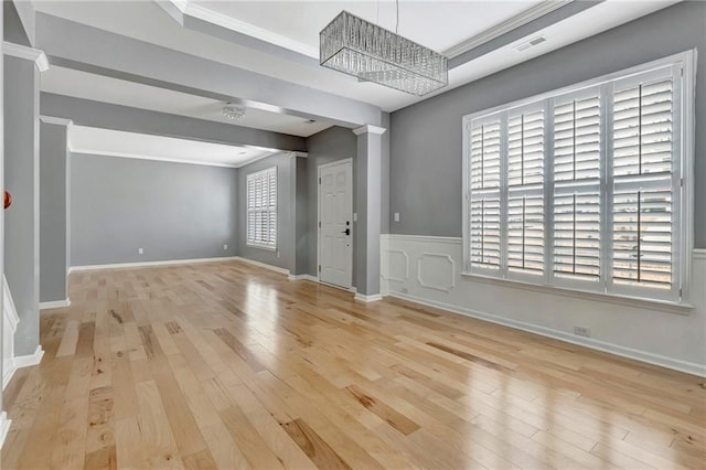 empty room featuring decorative columns, crown molding, light wood-type flooring, and an inviting chandelier