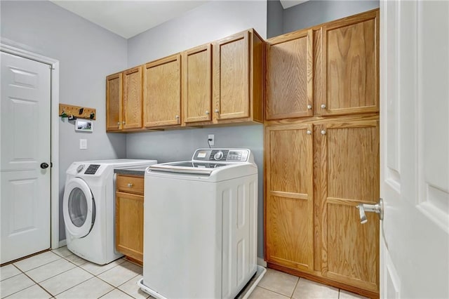 clothes washing area with cabinets, light tile patterned floors, and washing machine and clothes dryer