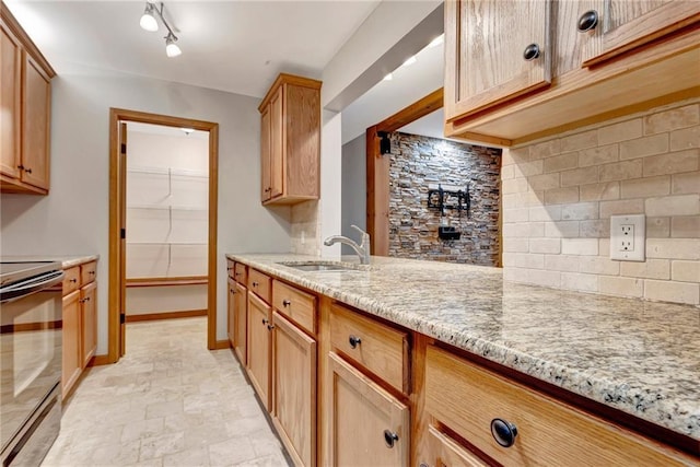 kitchen with stove, rail lighting, sink, decorative backsplash, and light stone countertops