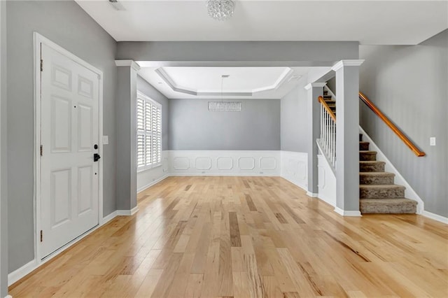 entrance foyer with a notable chandelier, a raised ceiling, and light wood-type flooring