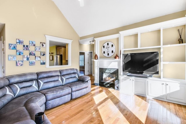 living room featuring a premium fireplace, light hardwood / wood-style flooring, and high vaulted ceiling