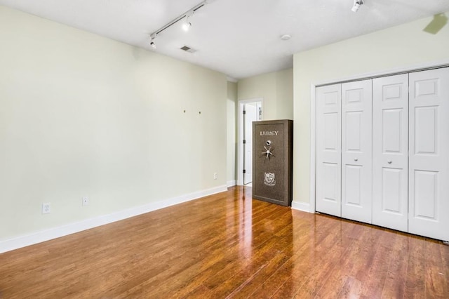 unfurnished bedroom with wood-type flooring, rail lighting, and a closet