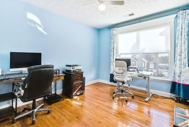 office space with a wealth of natural light, light hardwood / wood-style flooring, ceiling fan, and a textured ceiling