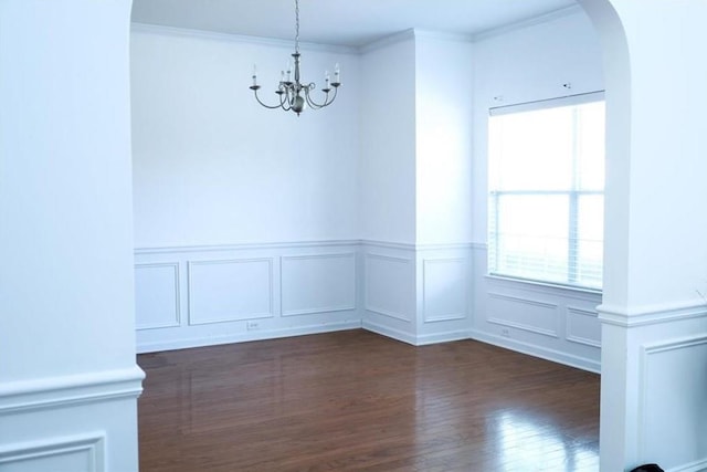 empty room with dark hardwood / wood-style flooring, crown molding, and a chandelier