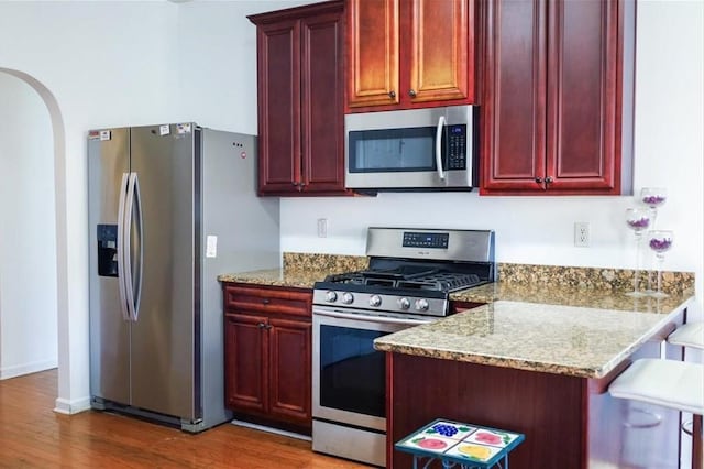 kitchen featuring light stone countertops, a kitchen bar, appliances with stainless steel finishes, and dark hardwood / wood-style flooring