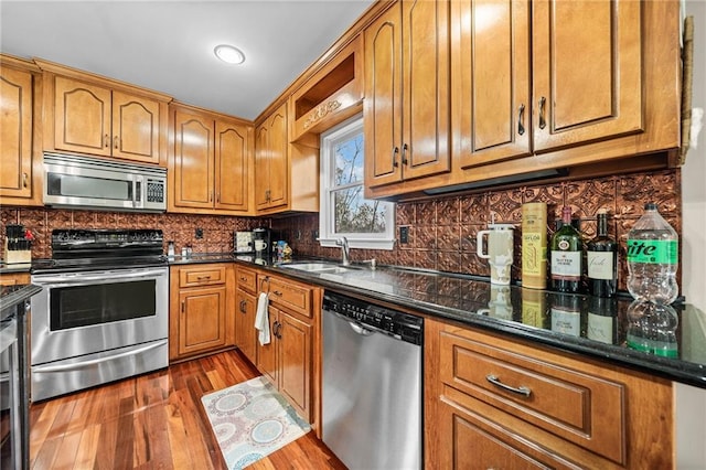 kitchen with appliances with stainless steel finishes, tasteful backsplash, sink, dark stone countertops, and dark hardwood / wood-style flooring