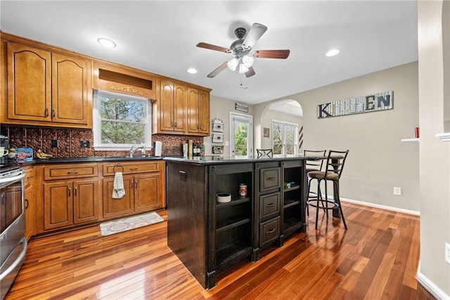 kitchen with ceiling fan, tasteful backsplash, wood-type flooring, stainless steel range oven, and a kitchen island