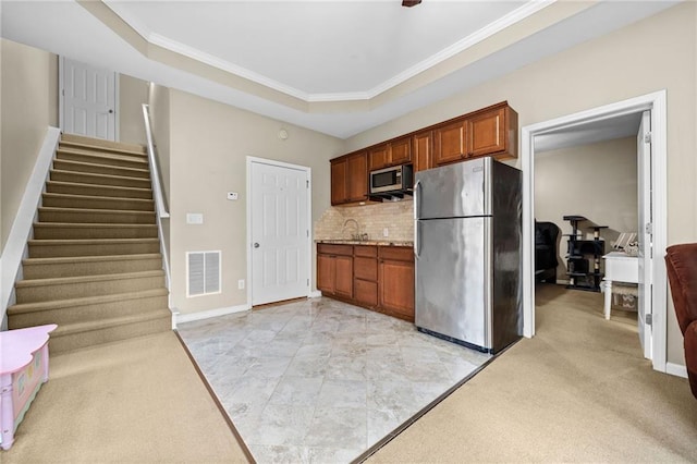 kitchen with sink, crown molding, appliances with stainless steel finishes, decorative backsplash, and a raised ceiling