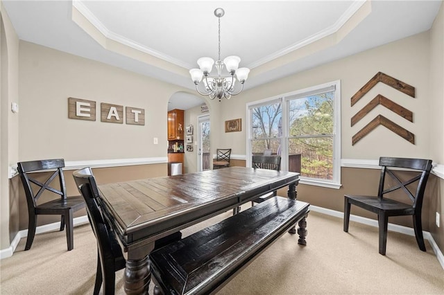 dining room with a chandelier, ornamental molding, a raised ceiling, and light carpet