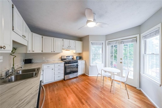 kitchen featuring stainless steel gas range, a sink, extractor fan, light countertops, and light wood-type flooring