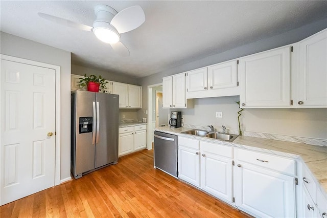 kitchen with a sink, stainless steel appliances, light wood-style floors, white cabinets, and light countertops