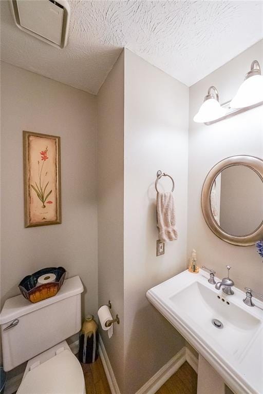 half bath featuring a textured ceiling, toilet, baseboards, and a sink