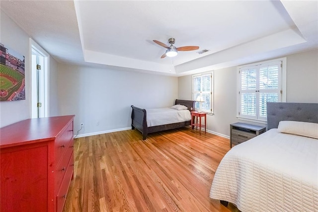 bedroom featuring light wood finished floors, visible vents, a raised ceiling, and baseboards