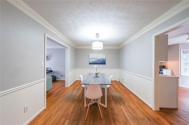 dining area featuring a textured ceiling, baseboards, light wood finished floors, and ornamental molding