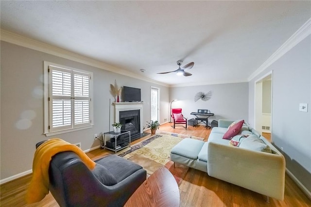 living area with ornamental molding, a fireplace, baseboards, and wood finished floors