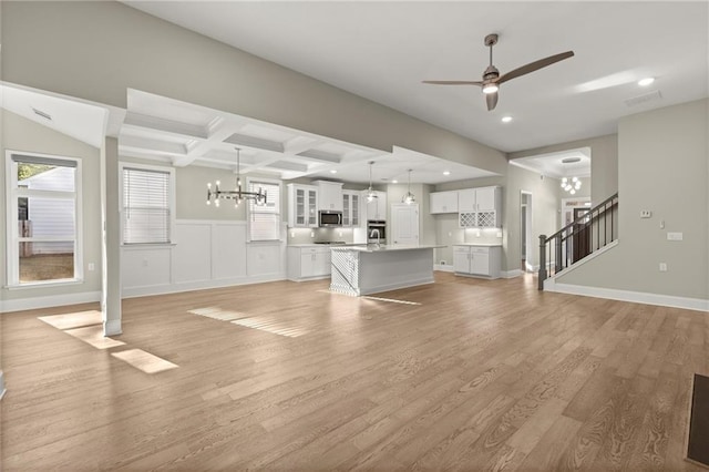 unfurnished living room with beamed ceiling, light wood-style flooring, stairs, and ceiling fan with notable chandelier