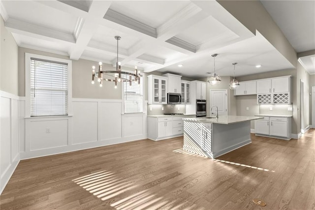 kitchen with light countertops, a sink, stainless steel microwave, beam ceiling, and a chandelier