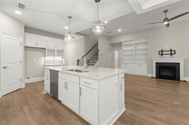 kitchen with light wood-style flooring, a sink, a center island with sink, white cabinetry, and dishwasher