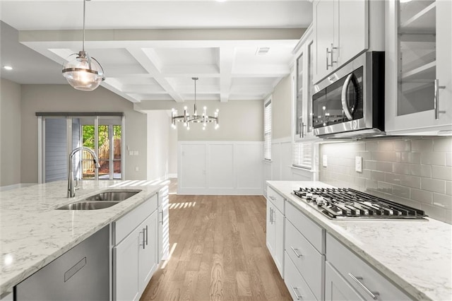 kitchen with stainless steel appliances, a sink, beamed ceiling, light wood-style floors, and hanging light fixtures