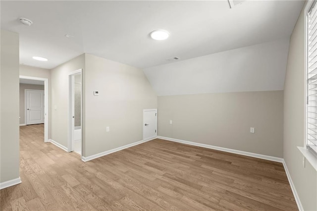 additional living space with vaulted ceiling, light wood-style flooring, visible vents, and baseboards