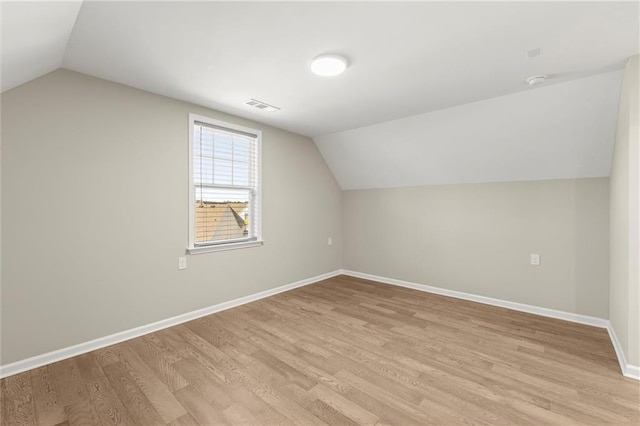 additional living space with vaulted ceiling, light wood-style floors, visible vents, and baseboards