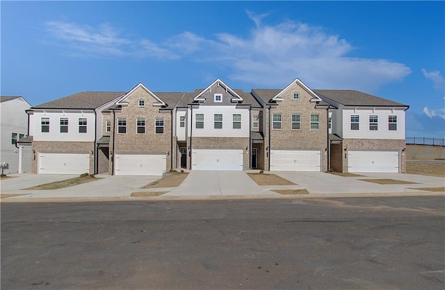 view of property with concrete driveway, a residential view, an attached garage, and brick siding