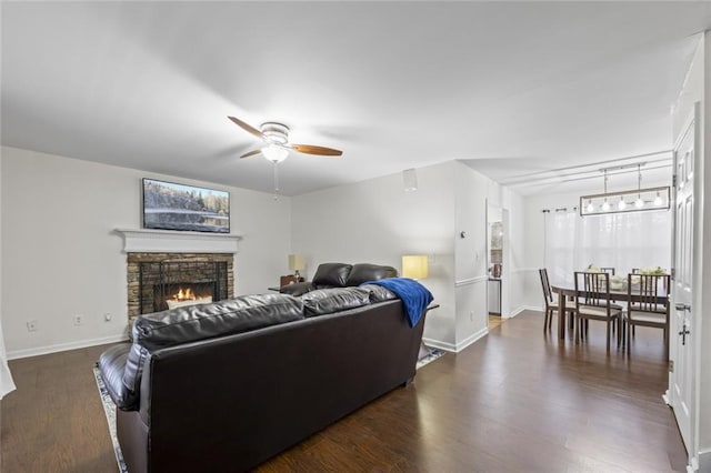 living room featuring a stone fireplace, ceiling fan, and dark wood-type flooring