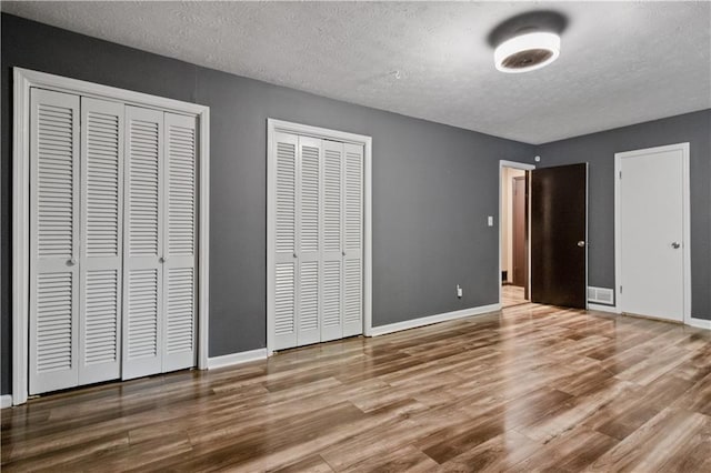 6945 Butner Rd, Atlanta, GA 30349 - unfurnished bedroom with baseboards, a textured ceiling, multiple closets, and wood finished floors