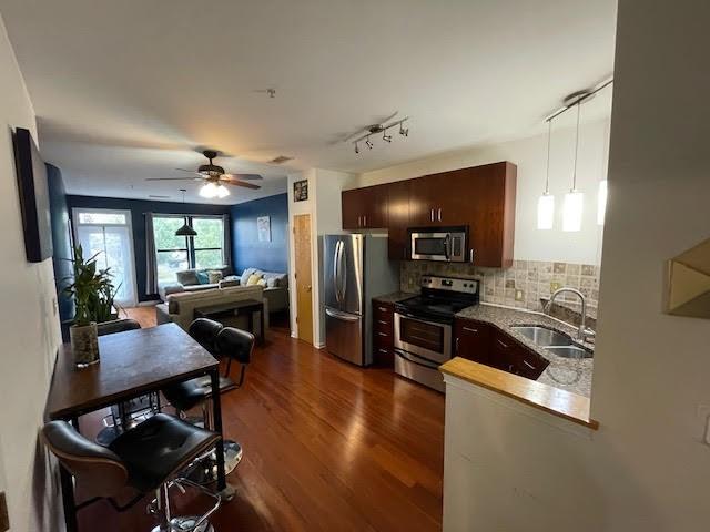 kitchen featuring appliances with stainless steel finishes, dark brown cabinetry, dark hardwood / wood-style floors, decorative backsplash, and sink