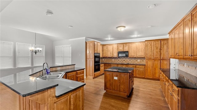 kitchen with a large island, light wood-style flooring, decorative backsplash, a sink, and black appliances