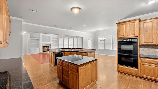 kitchen with light wood-style flooring, a kitchen island, black appliances, a glass covered fireplace, and crown molding