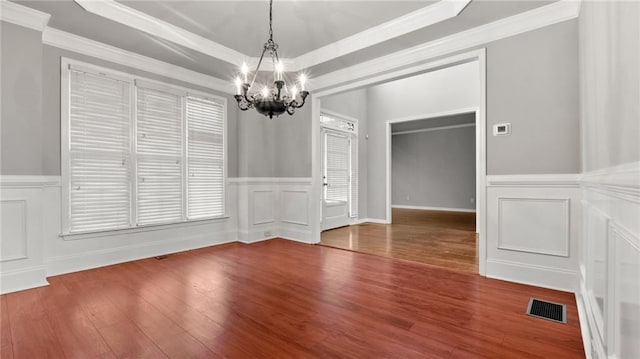 unfurnished dining area featuring a decorative wall, a notable chandelier, wood finished floors, visible vents, and a raised ceiling