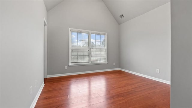 empty room featuring high vaulted ceiling, visible vents, baseboards, and wood finished floors